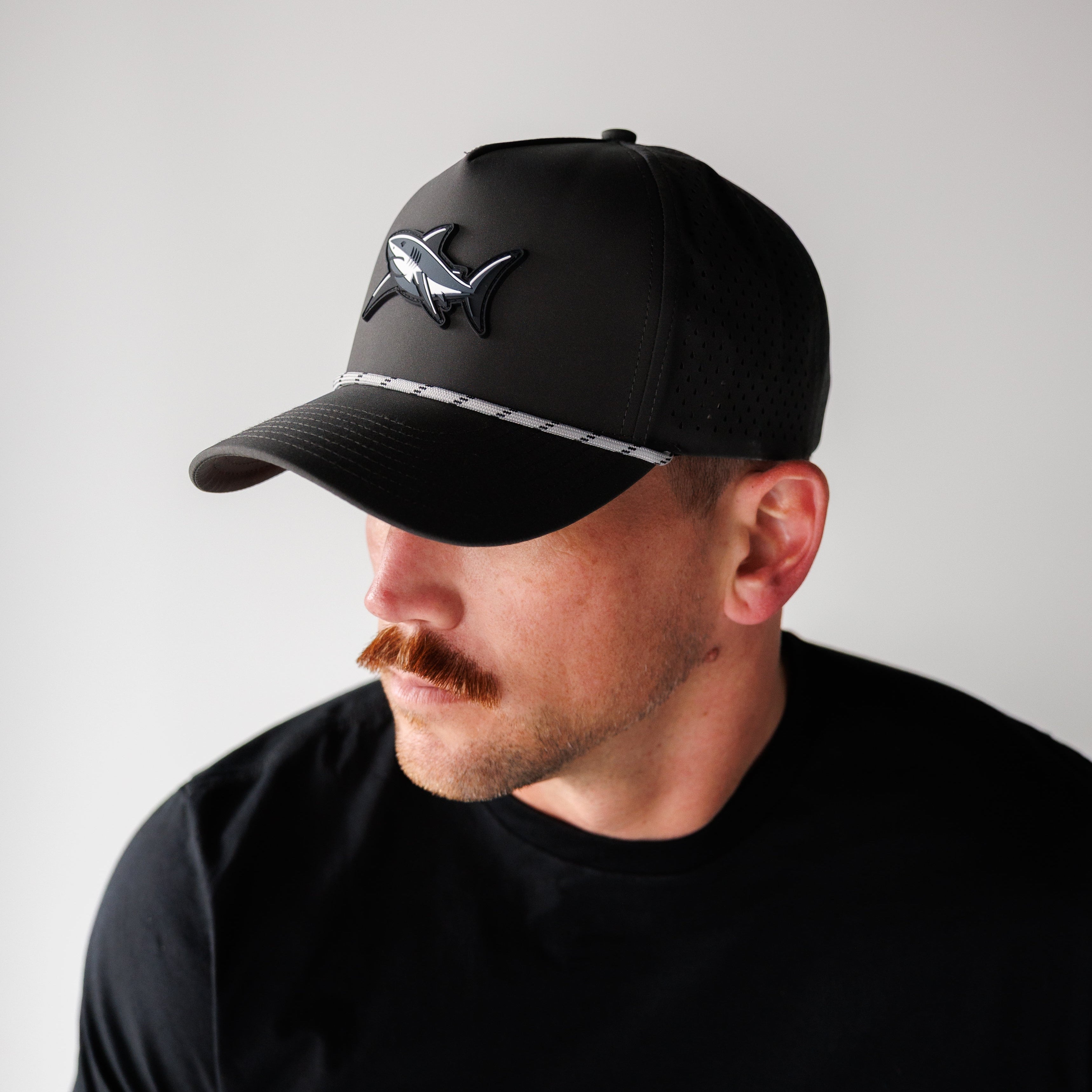 Man wearing a black cap with a logo on a plain background
